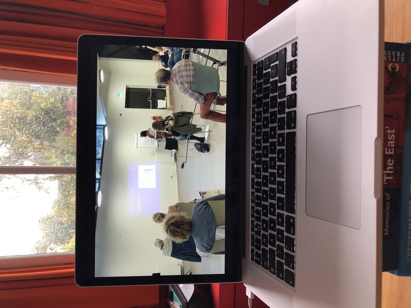 Symposium eenzaamheid. In beeld zijn een laptop en op het beeldscherm een locatie met meerdere mensen