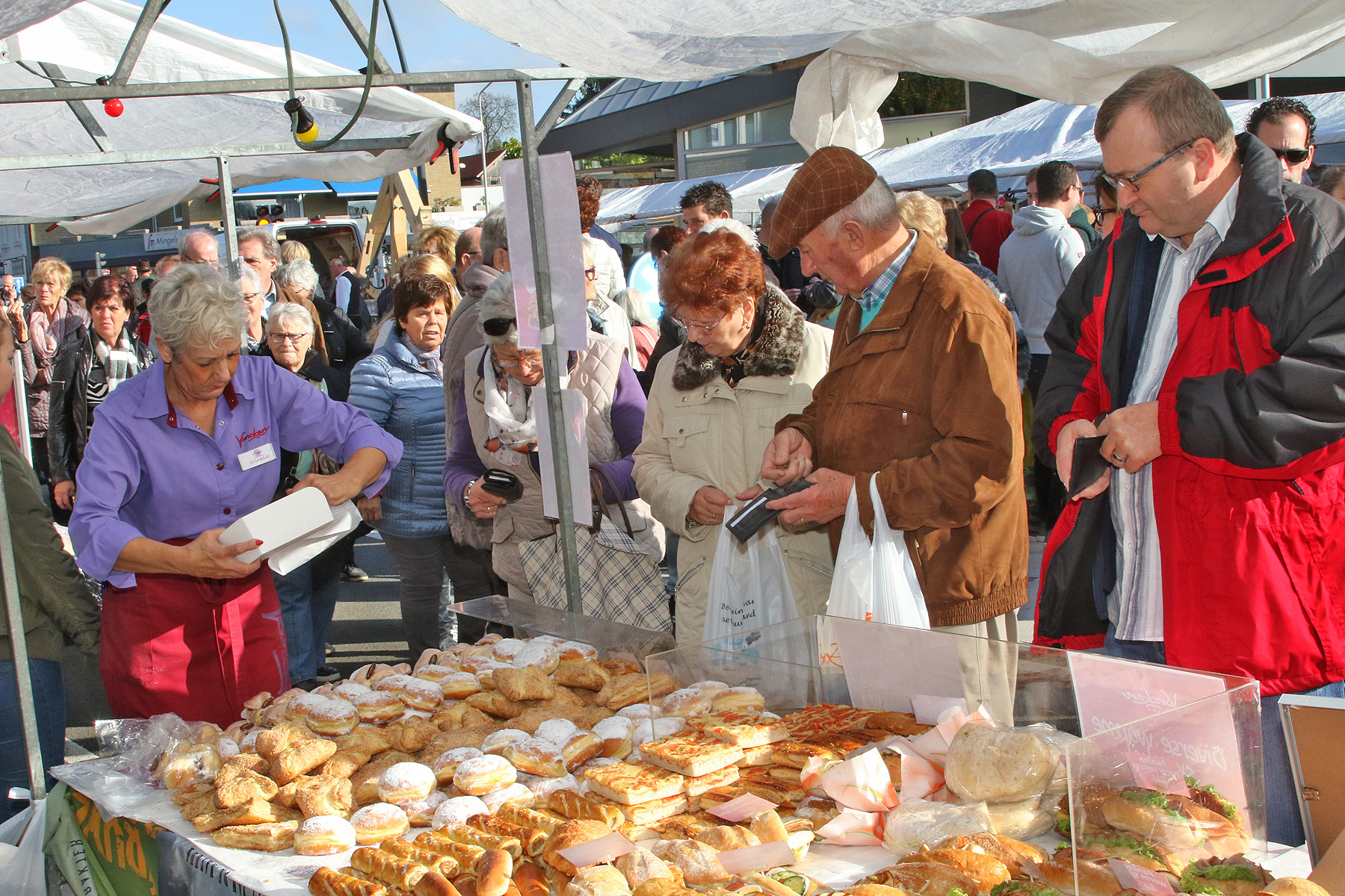 Diverse mensen staan voor marktkraam met gebakjes
