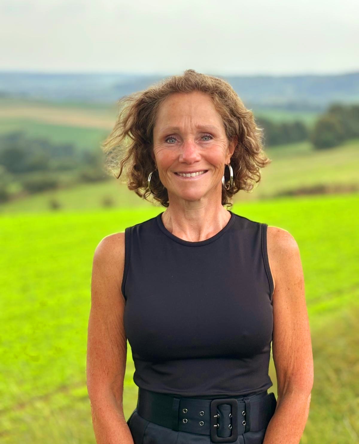 Trouwambtenaar Ingrid Smeets. Zij staat in een groen wijds landschap en lacht. 